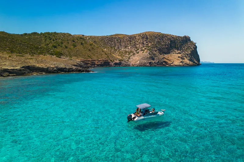 Lancha fondeada en agua turquesa frente al cabo